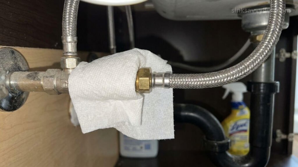 checking kitchen sink supply line leak Wrapping a dry paper towel around the metal nut of a braided water supply line to check for active leaks under the sink