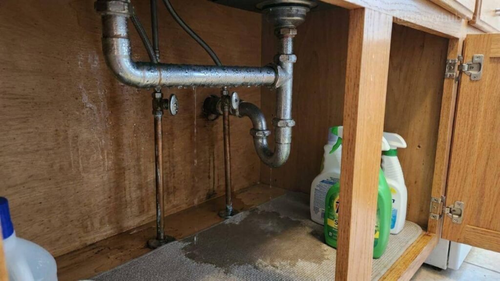 Cold metal water supply lines sweating condensation drops, causing a damp smell under the kitchen sink.