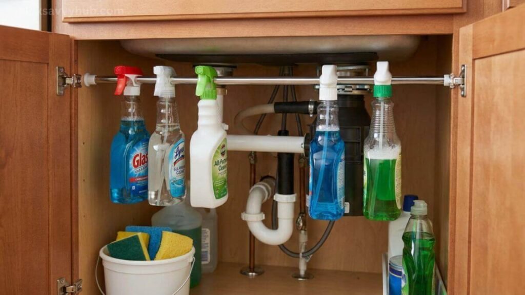 Hanging spray bottles on a metal tension rod to organize the awkward space around kitchen sink pipes